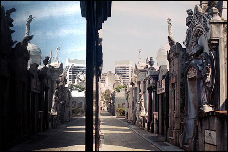 Looking down a street of tombs in Recoleta Cemetery, reflected in polished stone on the left.